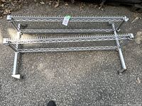 Three metal wire shelving sections lying on pavement showing horizontal frames and wire mesh surfaces.