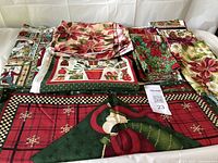 Top-down view of assorted folded Christmas fabrics and unfinished placemats showing poinsettia, gift, and ornament patterns.