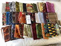 Overview of 34 quilting cotton fat quarters with diverse colors and patterns, neatly folded on a white surface.