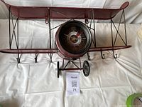 Full view of red metal airplane wall hanger showing six hooks underneath and clock integrated in front.