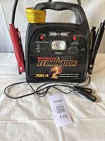 Front view of Motomaster Eliminator 700A Mobile Booster Pack with clamps and 12V cable laid in front.