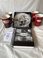 Photo showing 4 Tim Hortons mugs, Royal Doulton limited edition plate in box wrapped in plastic, and a black and white Tim Hortons notebook with spiral binding