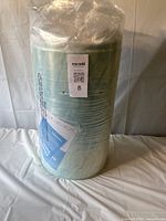 Photo showing mattress topper rolled and sealed in clear plastic packaging with MaxSold lot tag attached.