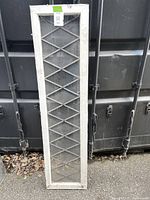 Full frontal view of the vintage leaded pane window against a dark background showing the diamond lattice pattern in the glass and painted wood frame.