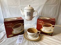 Image showing a cream-colored Tim Hortons branded teapot with lid centered and two boxed Tim Hortons teacup and saucer sets on either side, all displayed against a white background.