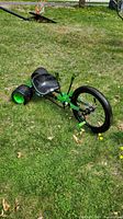 Side angle view of the green Huffy Green Machine kids tricycle on grass showing the three wheels, black seat, and front pedals.