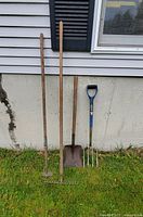 Four outdoor garden tools leaning against a wall on grass showing overall lot contents