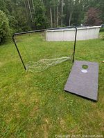 Soccer net frame with loose net and cornhole board on grass outdoors