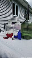 Vintage glass bottles including large clear carboy bottles, a large green textured bottle, small cobalt blue bottle, and a red glass slipper