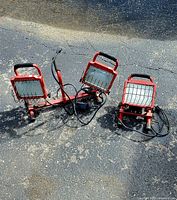 Photo of two portable work lights outdoors on asphalt ground, one double light on stand and one single light.