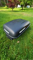 Black Yakima Spacecadet hard shell car top carrier shown on grass outdoors with visible branding and aerodynamic shape.