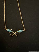 Close-up of pendant showing two stylized fish shapes with turquoise enamel on black background