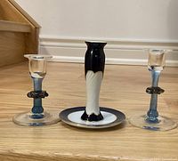 Photo showing two clear glass candle holders with blue stems and one black and white porcelain candle stand with plate
