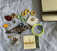 Top-down view of assorted small items including colorful plastic rings, pins, metal chains, and a small figurine spread out on a surface alongside a partial view of a laptop
