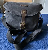 Front view of gray canvas BAGSMART camera bag with black shoulder strap and leather buckle flap closure.
