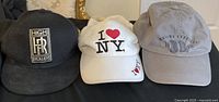 Photo of three caps: black High Roller, white I Love NY, and grey Baja Republic caps on a black surface.