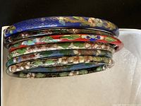 Six colorful cloisonné bangles stacked showing floral enamel designs and varying colors including blue and red.
