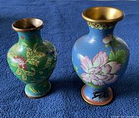 Photo of both cloisonné vases from the front showing the floral and bird enamel designs on blue and green backgrounds.
