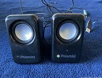 Front view of two Polaroid computer speakers showing speaker cones, front logos, and cables attached