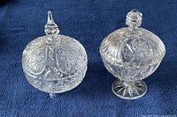Two crystal candy jars placed side by side on a dark blue cloth, showing the detailed star and fan cut patterns and their respective lids.