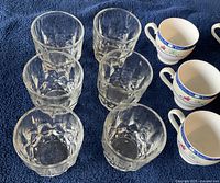 Six clear textured glass tumblers arranged on a dark blue fabric background.