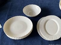 Photo showing 2 round dinner plates, 1 oval plate and 1 bowl laid on dark blue fabric