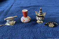 Four display items arranged on blue fabric: ceramic vase, decorative jar, metal item, and bug-shaped clock.