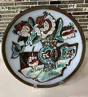 Front view of the decorative plate showing the floral design with abstract flowers in green, white, brown, and red colors.