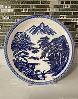 Front view of one blue and white Japanese display plate with mountain and water scene, geometric blue rim pattern