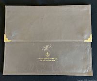 Front view of brown synthetic leather document holder with gold-tone corner protectors and stamped gold logo.