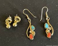 Two pairs of earrings displayed on black fabric background, one pair dangle with turquoise and coral stones and gold accents, one pair silver-toned stud knot with ball drop.