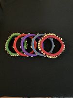 Top view of 5 assorted color cotton-wrapped bangles decorated with small gold and purple beads