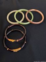 Top view of five fashion bangles arranged on black background showing translucent and dark bangles