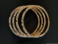 Four circular fashion bangles decorated with faux pearls, gold beads and occasional red beads on a black background.