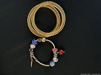 Two gold-tone bangles and one silver charm bracelet resting on black background, showing overall lot contents.