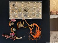 View of assorted fashion jewelry pieces including various earrings and a beaded necklace with tassels displayed on black surface.