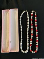 Two necklaces side by side on a black cloth background with a pink jewelry box lid next to them.