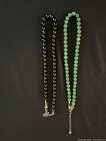 Two beaded necklaces laid flat: one black, one green, showing clasp and bead details.