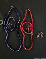 Two necklace sets and three pairs of earrings on black background: one dark blue beaded necklace with small matching earrings, and one red beaded necklace with two pairs of matching earrings.
