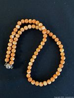 Single strand orange stone bead necklace coiled on a black background showing bead size and texture along with silver-tone clasp detail.