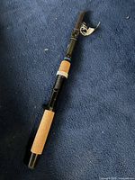 Folded black fishing rod with cork handle grips lying on a blue surface, showing the full length and reel seat.