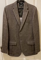 Full front view of the brown herringbone patterned Banana Republic jacket hung on a hanger, showing the overall design, pockets, and button closure.