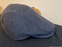 Gray men's flat cap placed on a black surface showing side and top view of hat material and shape.