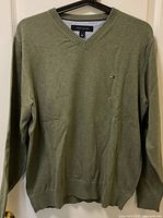 Olive green Tommy Hilfiger men's sweater on hanger, front view.