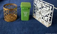 Front view of three items: gold metal holder, green mini trash bin with printed text, white floral metal organizer.