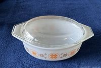 Photo of white ceramic Pyrex bowl with orange and brown starburst pattern and clear glass lid on top