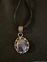 Front view of silver pendant featuring oval blue stone with decorative silver beads on black cord necklace.