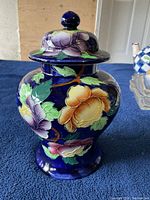 Front view of a deep blue ceramic vase with large colorful flowers, showing the vase's shape and floral painted details.