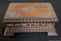 Photo of the vintage wooden box showing the intricate metal floral decorations on the lid and sides with scalloped edges and small feet.