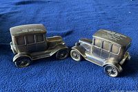 Two dark metal model cars on blue fabric, showing side and roof details with advertising text.